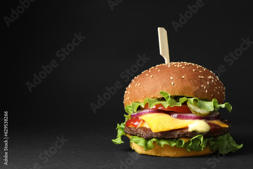 Delicious burger with beef patty and lettuce on black background, space for text