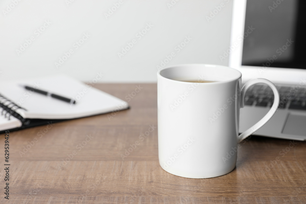 White ceramic mug with drink, notebook and laptop on wooden table at workspace, space for text White ceramic mug with drink, notebook and laptop on wooden table at workspace, space for text