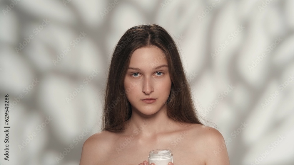 Appealing young girl model with long hair holding a small jar of cream Appealing young girl model with long hair holding a small jar of cream