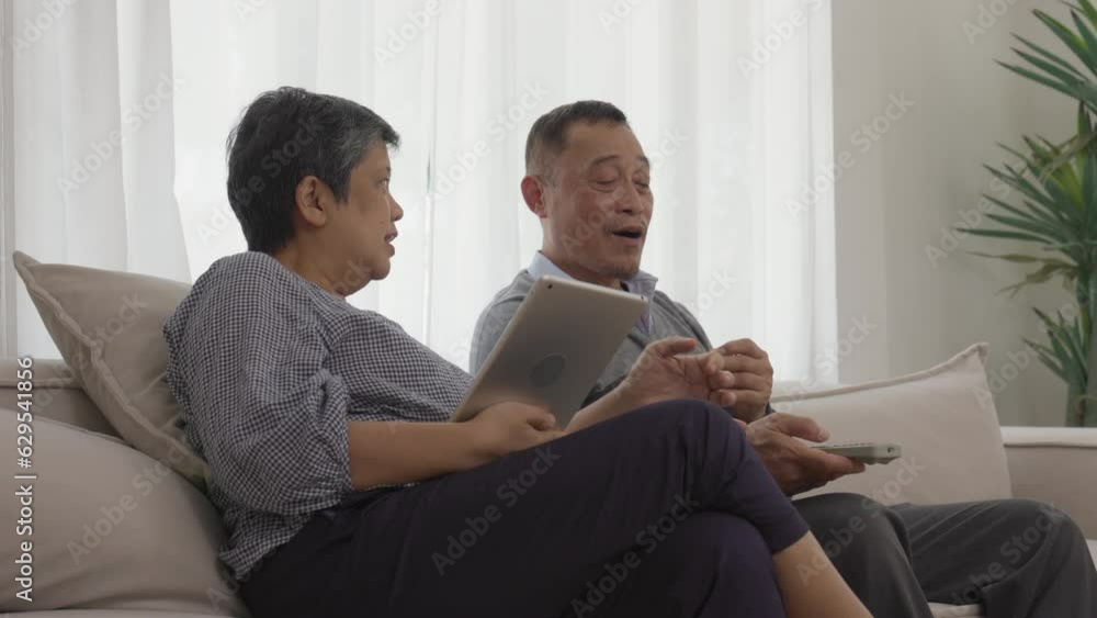 Happy Asian Senior Couple Enjoying TV and Tablet Time in Real Time Happy Asian Senior Couple Enjoying TV and Tablet Time in Real Time