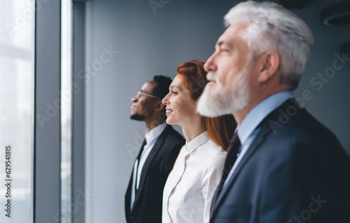 Multiracial coworkers looking through panoramic window at work