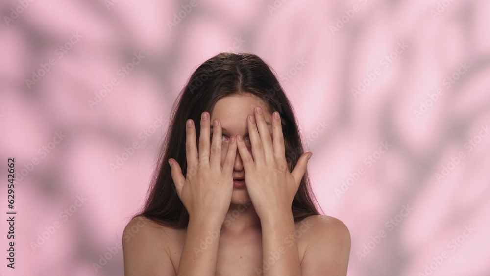 Beautiful brunette model with natural makeup hiding her face looking at the camera Beautiful brunette model with natural makeup hiding her face looking at the camera