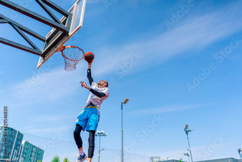 Tall guy basketball player jumps to the hoop with the ball in his hand to score a spectacular dunk during practice on the basketball court in the park