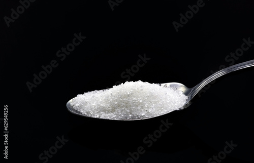 A small teaspoon with sugar, on a black background.