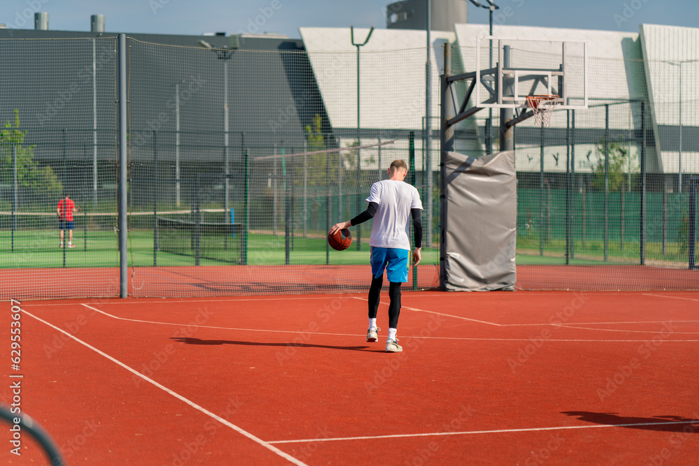 Fototapeta premium a Tall guy basketball player with the ball shows his dribbling skills during practice on the basketball court in the park 