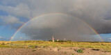 Himmel mit Regenwolken und Regenbogen über dem Strand der Ostsee auf Fehmarn in Schleswig-Holstein. Unter dem Regenbogen der Leuchtturm Westermarkelsdorf