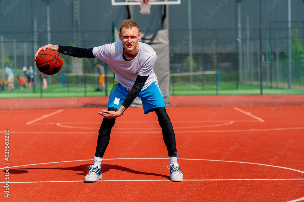 a Tall guy basketball player with the ball shows his dribbling skills during practice on the basketball court in the park 