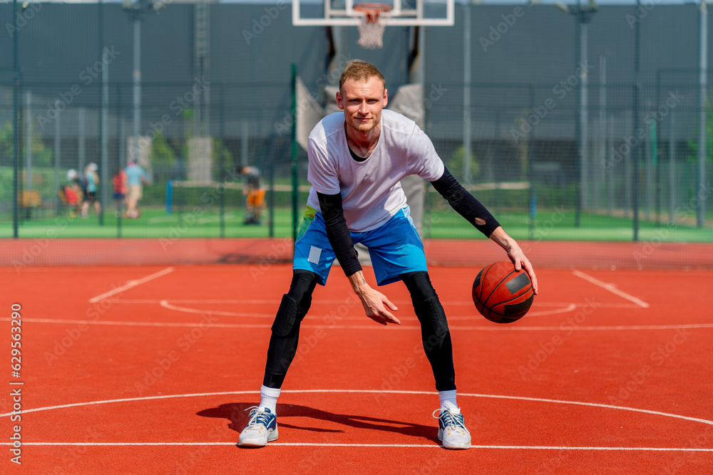 Obraz premium a Tall guy basketball player with the ball shows his dribbling skills during practice on the basketball court in the park