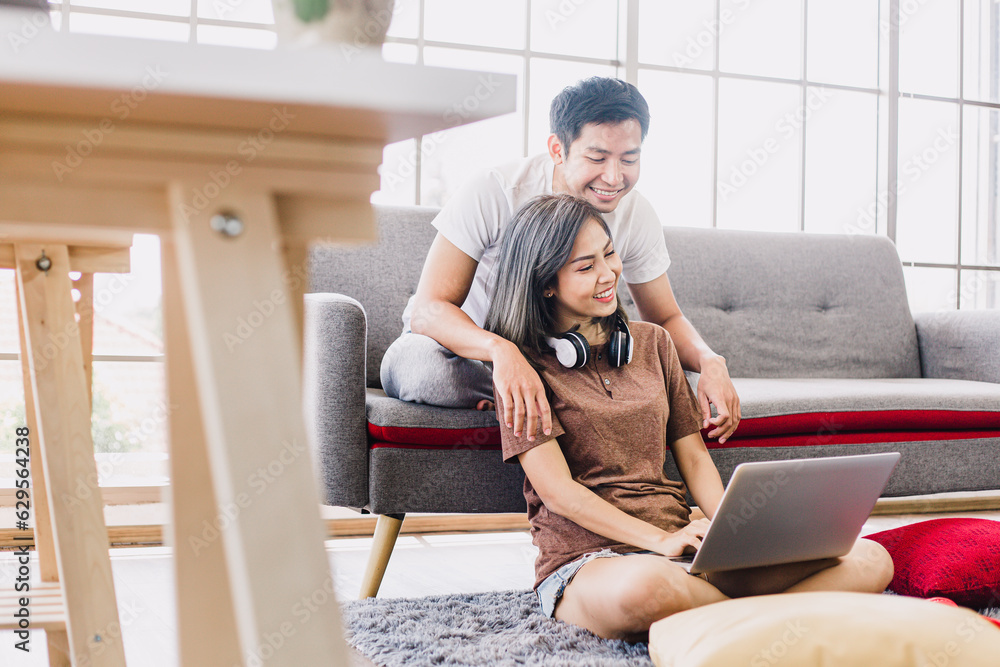 Happy Asian couple shopping online with laptop computer at home. Lovely couple making purchases online or booking in beautiful living room. Buying ordering products on the internet. Happy Asian couple shopping online with laptop computer at home. Lovely couple making purchases online or booking in beautiful living room. Buying ordering products on the internet.