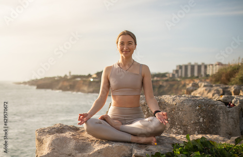 Positive millennial caucasian lady athlete in sportswear practices yoga in lotus position  meditates  enjoys rest