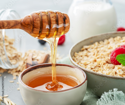 Honey dripping from wooden honey dipper. Oatmeal porridge at the background. photo