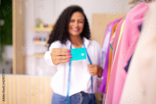 Latin woman dressmaker showing credit card at clothing showroom indoors