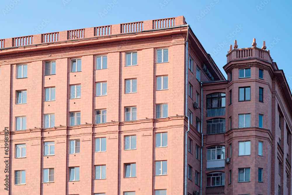 Part of classic real estate building or block of flats of pink color standing against blue sky in the center of modern city Part of classic real estate building or block of flats of pink color standing against blue sky in the center of modern city