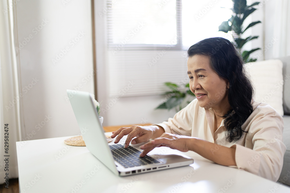 Fototapeta premium Middle age Asian woman Work from home. senior woman smiling Beautiful mature asian woman on laptop with technology concept