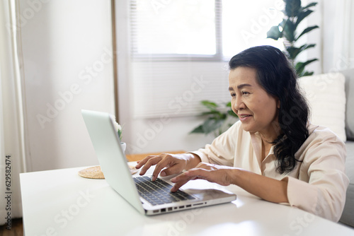 Middle age Asian woman Work from home. senior woman smiling Beautiful mature asian woman on laptop with technology concept © Charlie's