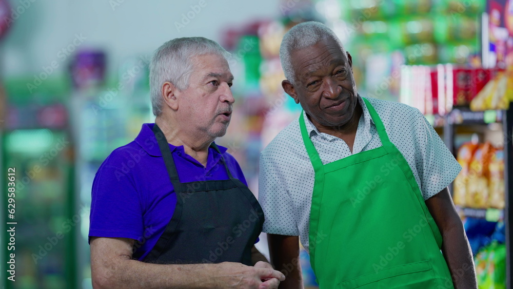 Senior diverse employees of grocery store discussing management of business at supermarket aisle wearing uniforms Senior diverse employees of grocery store discussing management of business at supermarket aisle wearing uniforms