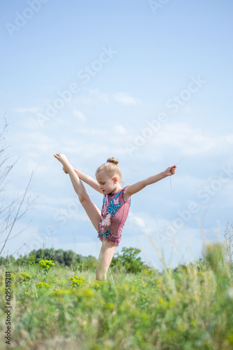 a gymnast in a beautiful swimsuit performs elements in nature © Galina