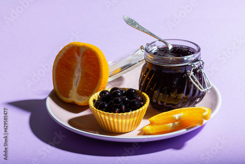 Obraz na płótnie Blackcurrant jam with orange in a glass jar on a lilac background. w salonie