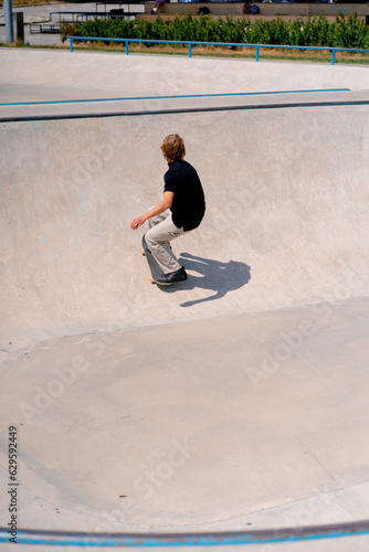 Young guy skateboarder with long hair skateboarding and doing tricks in the skate pool at the city skatepark 