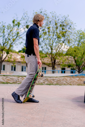 A young guy skateboarder stands in a skatepark with a skateboard in his hand before he starts skateboarding 