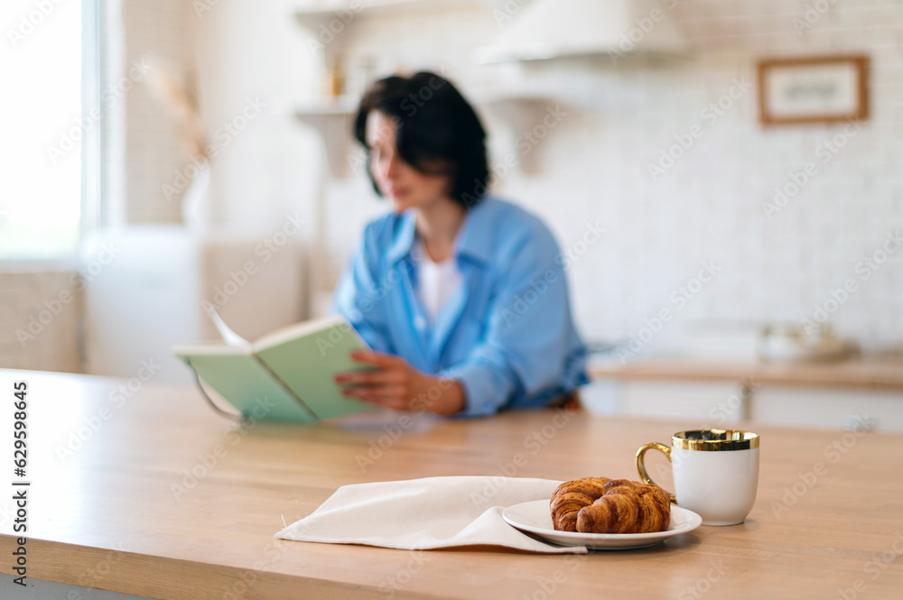 Croissants and cup with coffee against reading woman on background Croissants and cup with coffee against reading woman on background