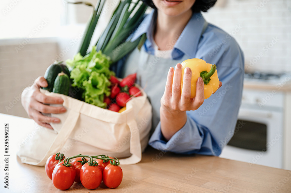 Selective focus on housewife hand holding yellow pepper, unpacking vegetables
