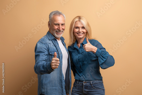 Obraz na płótnie Positive elderly couple showing thumb up on beige background