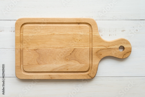 Top view of unused brand new brown handmade wooden cutting board on white wooden table background.