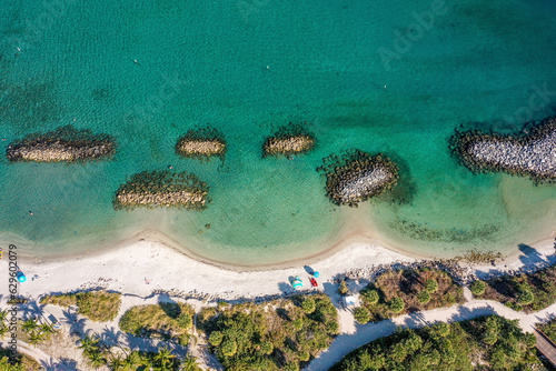 Aerial view of rock barriers on by the shoreline in clear blue waters, white sand and people on the beach of Peanut Island Park, Florida, United States. photo