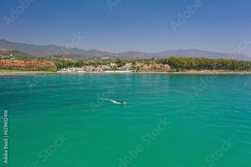 Aerial view of a person with jet ski on clear blue waters on a sunny day with mountains on the background in the city of Estepona, Málaga, Andalusia, Spain. photo