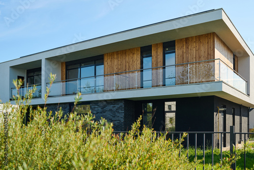 Side view of two storey cottage with group of windows and balcony on second floor situated in rural environment