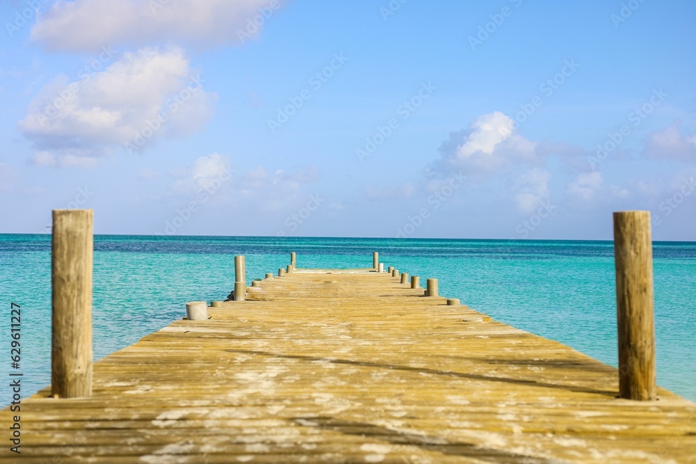 a pier leading into a vast turquoise ocean at the end of a beach