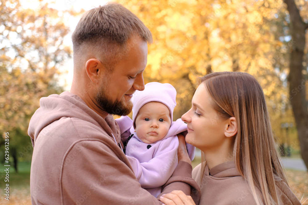 Young mother and father are walking with a newborn baby in the autumn park. Parents in identical tracksuits smile and look at the child Young mother and father are walking with a newborn baby in the autumn park. Parents in identical tracksuits smile and look at the child
