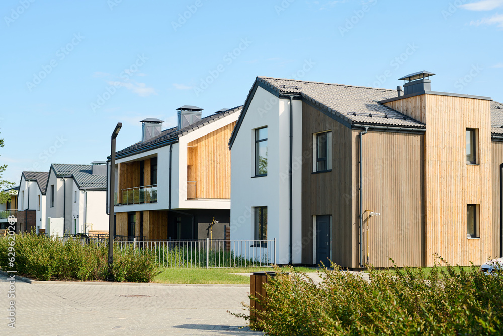 Two small houses with front yards with fencing and green bushes standing next to one another against clear blue sky