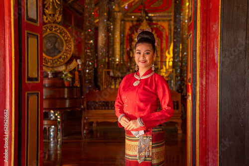 Portrait of young Asian woman wear Thai Lanna traditional dress stand in front door of ancient building look like temple and she stand with look at camera also smile.