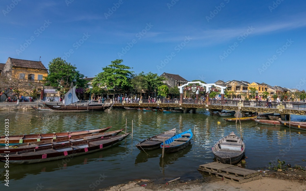 several boats are tied up on a river bank near a bridge and houses