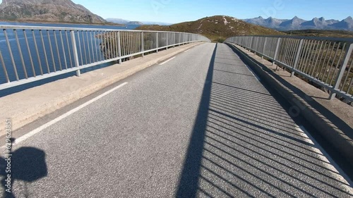 Cyclist riding over a narrow bridge, view of bay and the Seven Sisters, Helgeland, Heroey, Kystriksveien, Norway, Europe photo