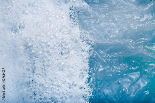 white cosmetic foam texture on blue water background. Bath foam. Cleanser, shampoo bubbles, wash - liquid soap, shower gel, shampoo. Cosmetics banner