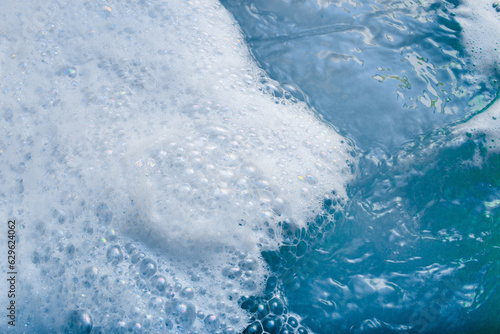 white cosmetic foam texture on blue water background. Bath foam. Cleanser, shampoo bubbles, wash - liquid soap, shower gel, shampoo. Cosmetics banner