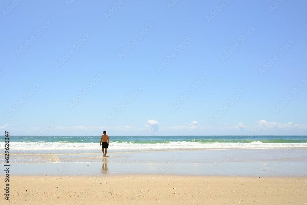 Man walking across a sandy beach, overlooking a picturesque ocean, Noosa North Shore Beach