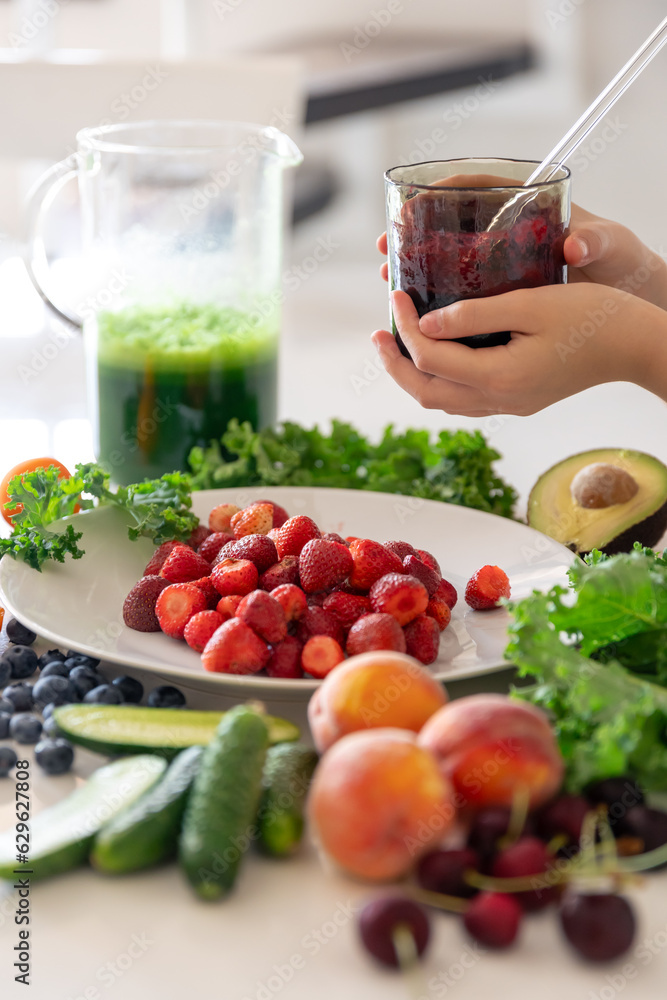 A glass of smoothie from berries in a child's hand at home in the kitchen. A glass of smoothie from berries in a child's hand at home in the kitchen.
