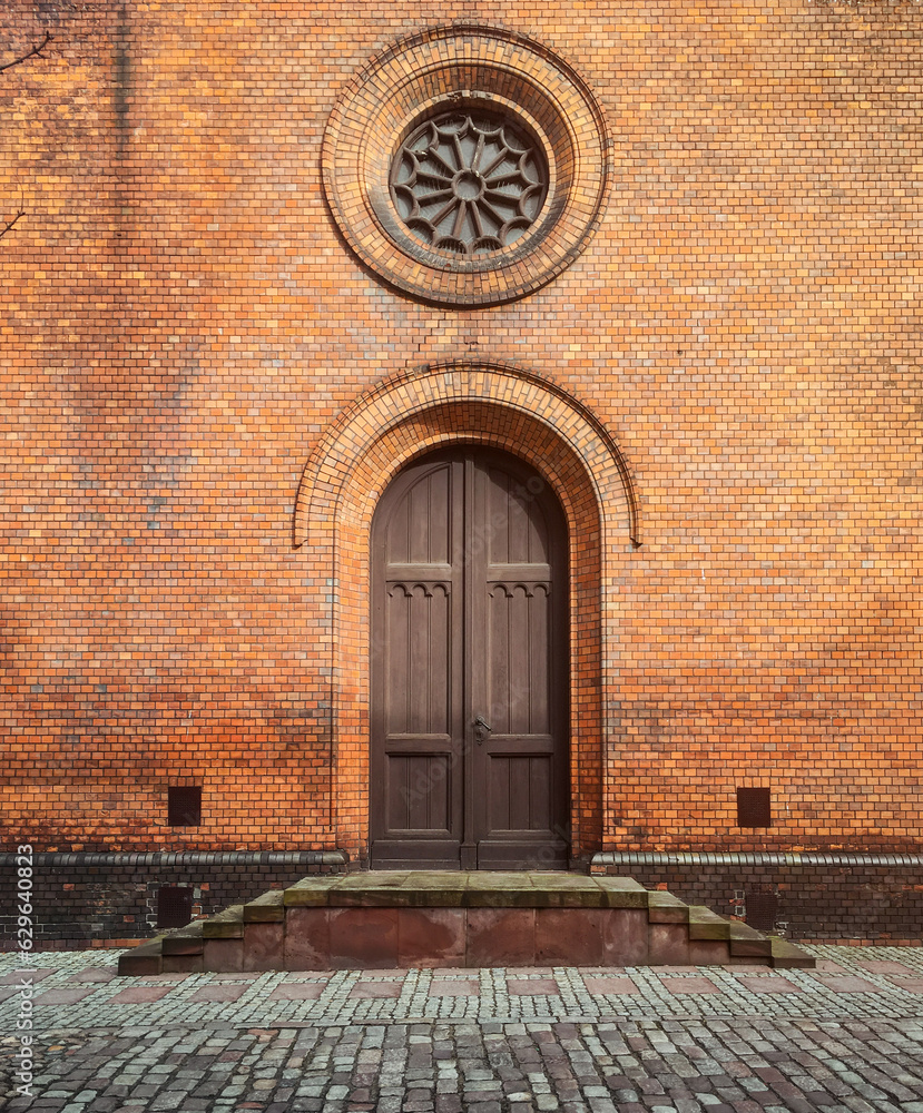 Side facade entrance into catholic church. Veranda porch with a wooden door and round rosette window above it