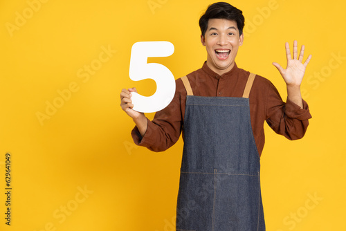 Fotografie Restaurant owner sme young Asian man holding number 5 or five isolated on yellow