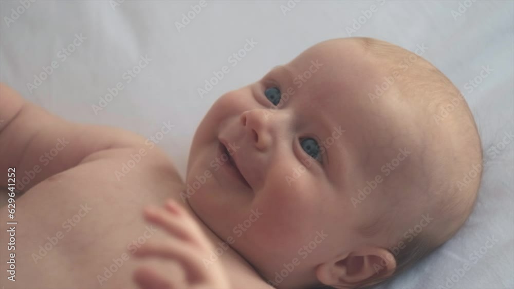 Portrait of smiling cute newborn baby son lying on comfortable white bed at home. Adorable smiling infant boy rests on cozy bedsheets in room, Infancy, healthcare and pediatrics, babyhood concept
