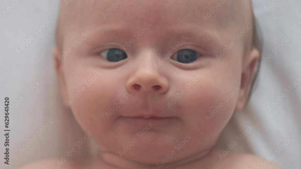 Close up portrait of pretty newborn baby lying down alone on comfy white bed at home. Adorable smiling infant boy rests on cozy bedsheets, Infancy, healthcare and paediatrics, babyhood concept Close up portrait of pretty newborn baby lying down alone on comfy white bed at home. Adorable smiling infant boy rests on cozy bedsheets, Infancy, healthcare and paediatrics, babyhood concept
