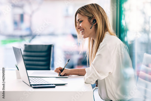 Elegant beautiful business woman doing videocall with laptop while talking with earphones in a modern startup