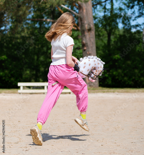 Girl jumping on hobby horse. Champion. Horse sport. Summer light. Green outdoor trees background. The Cavaletti route. Child sport. Banner photo