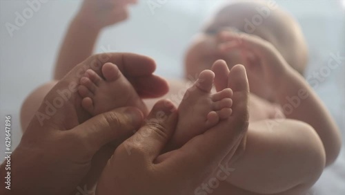 Selective focus of young father making baby massage lying on comfy white bed at home, loving daddy massaging infant bare foot, preventive massage for newborn, dad stroking baby feet with both hands