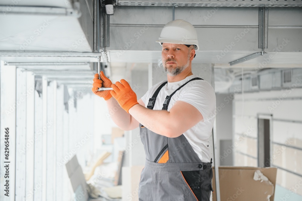 Man setting up ventilation system indoors. A male worker installs air ventilation pipes in a new office building. Man setting up ventilation system indoors. A male worker installs air ventilation pipes in a new office building.