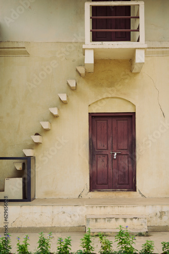 Wall with support pillars protruding with cream walls and brown door locked with a padlock